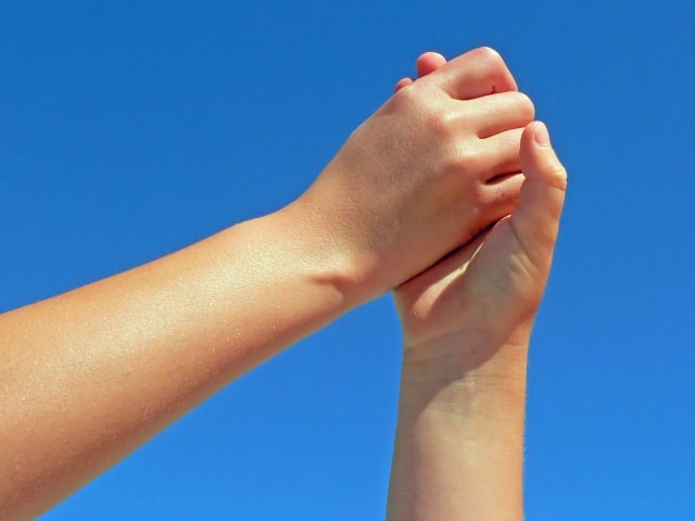 hands clasped together in front of a blue sky