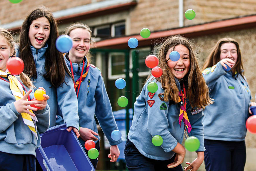 Guides in front of a building throwing coloured plastic balls