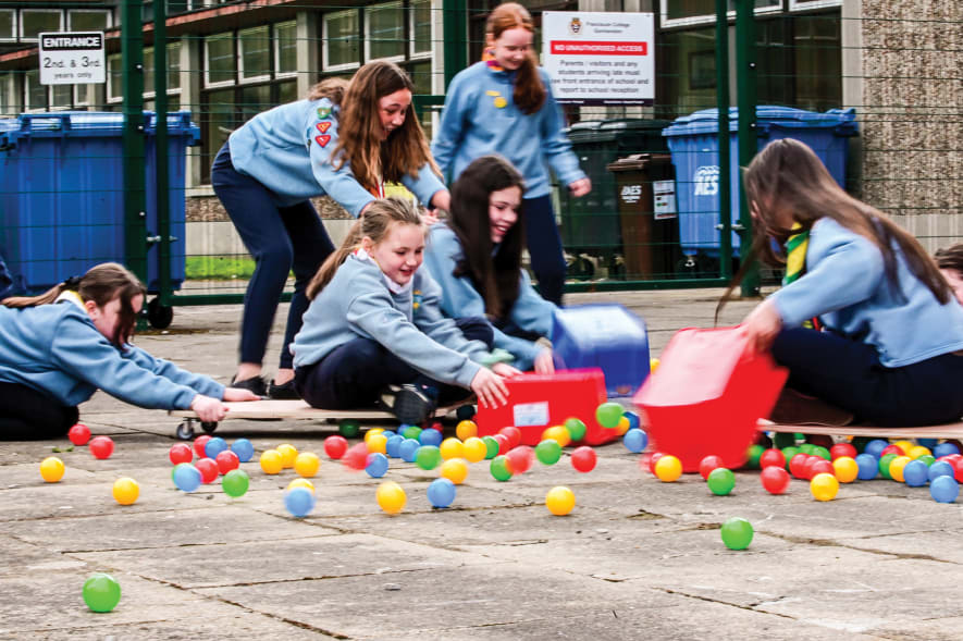 Girls on small trollys scooping up plastic balls in life sized Hungry Hippos game